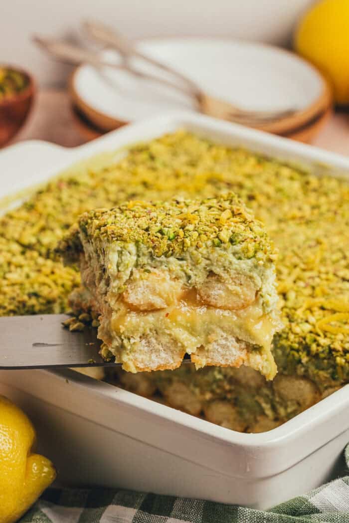 A slice of pistachio tiramisu cake being lifted out of the cake pan.