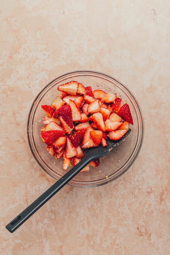 A bowl of fresh strawberries chopped with a spatula.