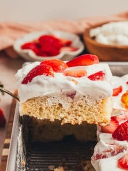 A slice of cake with strawberries is being lifted out of a cake pan.