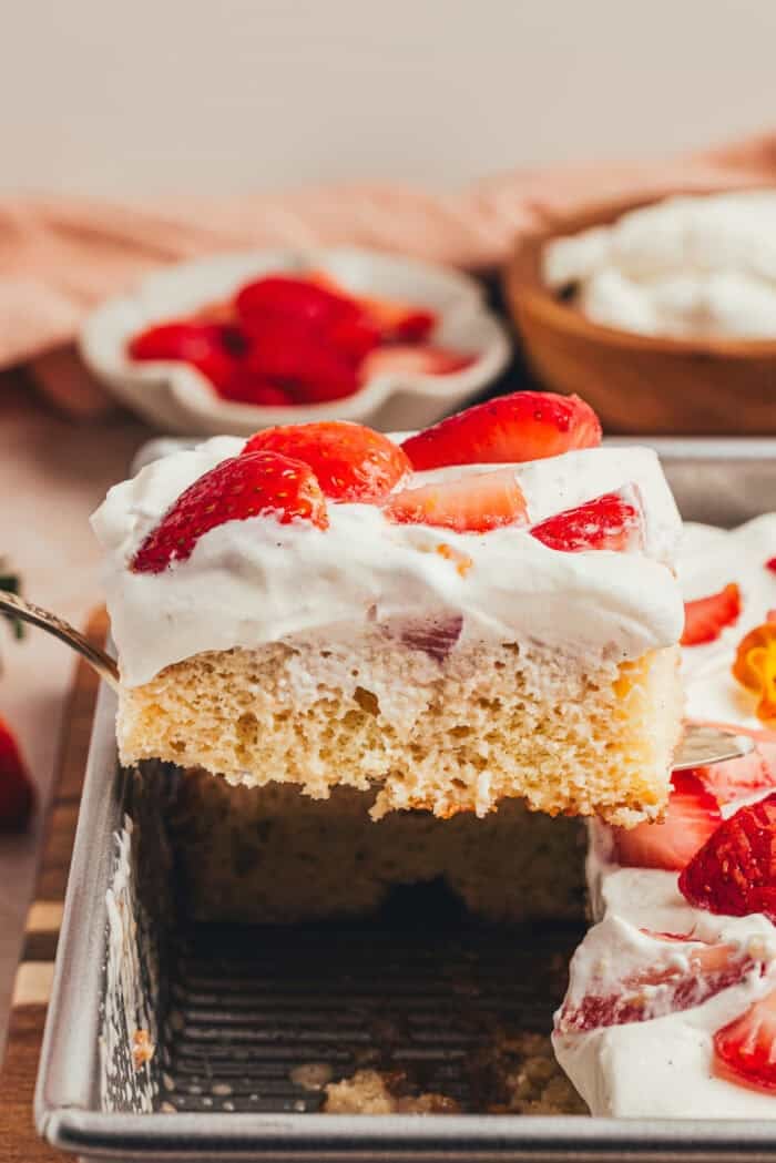 A slice of cake with strawberries is being lifted out of a cake pan.