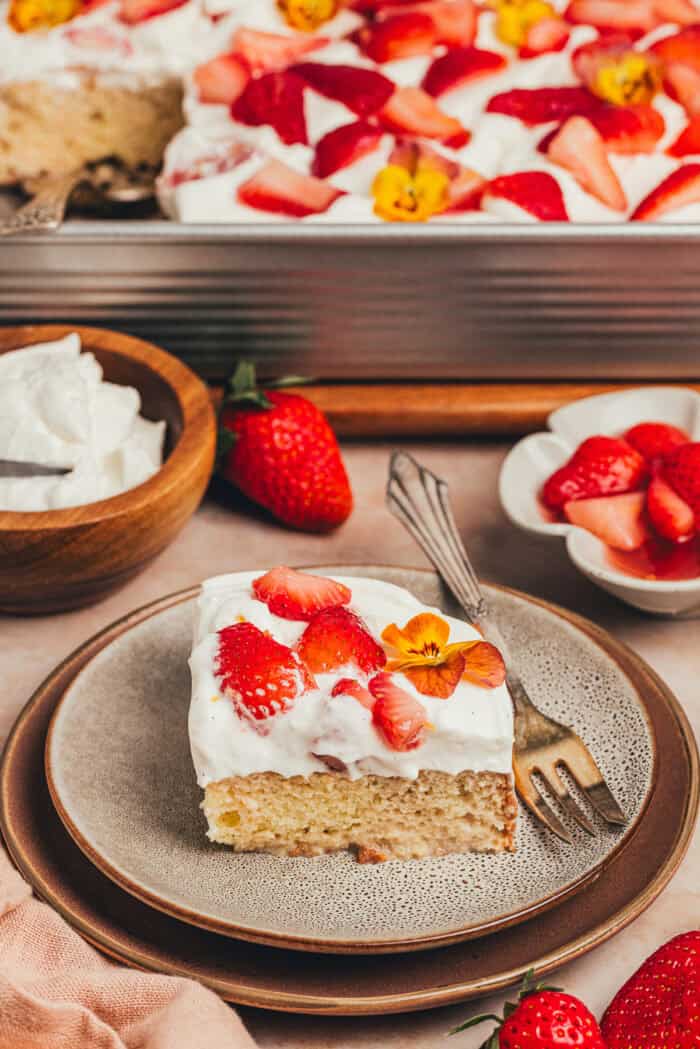 A slice of strawberry tres leches cake on a plate with a fork beside it.