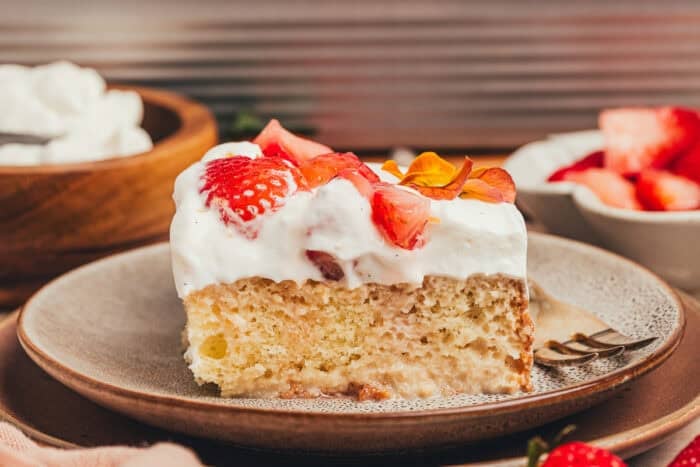 A slice of strawberry tres leches cake on a plate with a fork beside it.