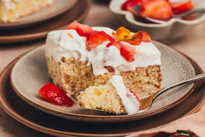 A slice of strawberry tres leches cake on a plate with a fork taking a bite out of the cake.