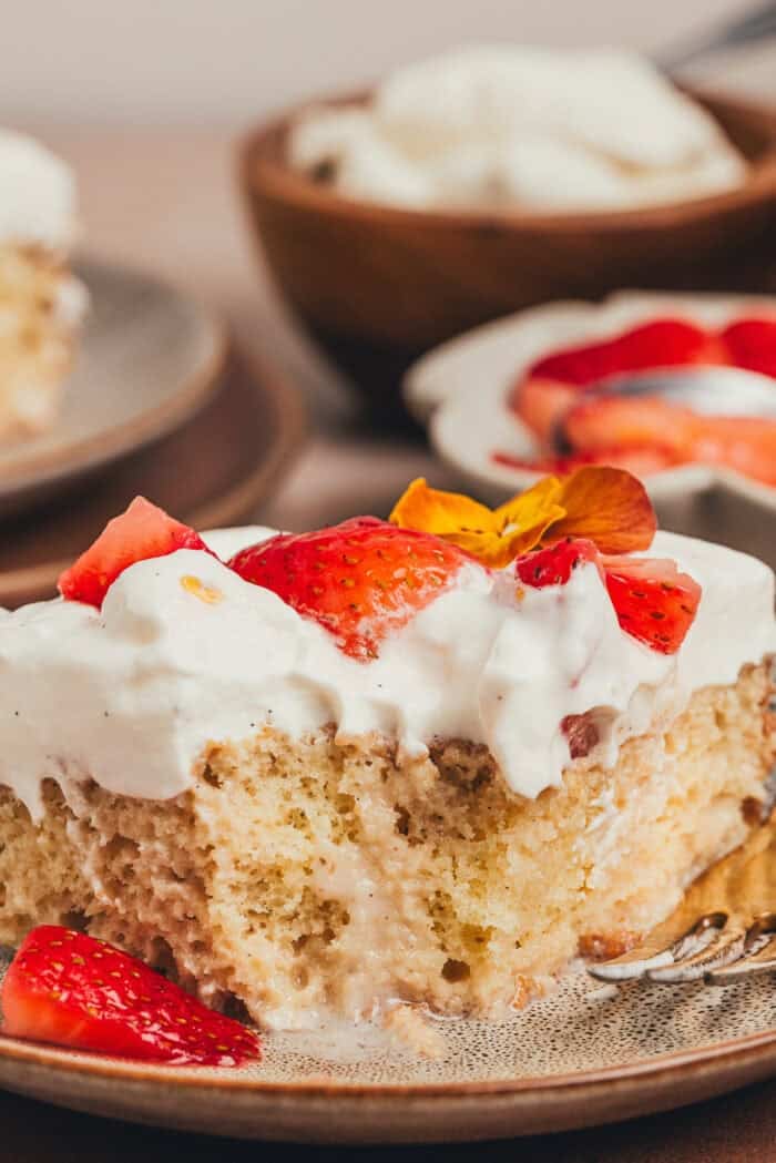 A slice of strawberry tres leches cake on a plate with a fork taking a bite out of the cake.