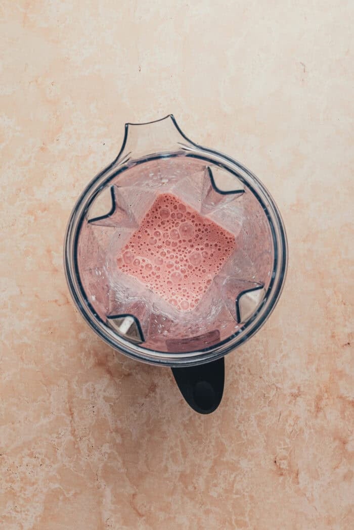 A blender with the ingredients used to make homemade strawberry milk.