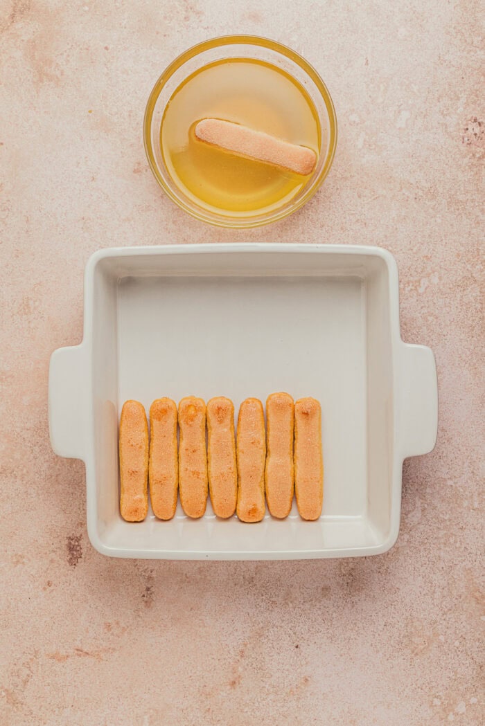 A square dish with the lady fingers dipped into a syrup and placed on the bottom of the dish.