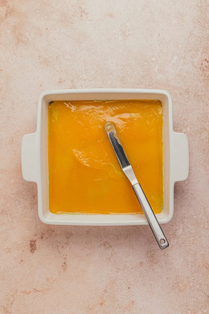 A square dish with the first layer of the lemon pistachio tiramisu that has the lemon syrup.