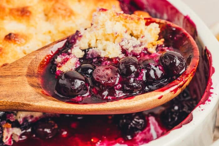A spoon lifting the blueberry filling out of the cobbler.