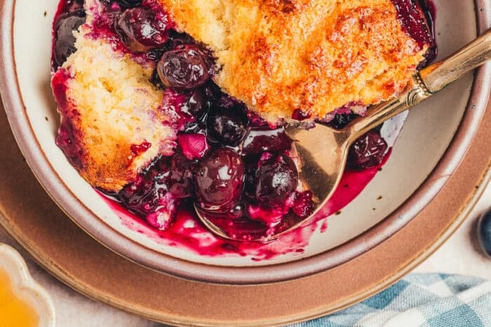 A bowl with a serving of blueberry cobbler and a spoon.