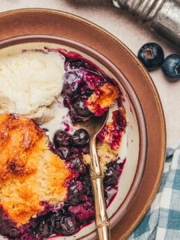 A bowl with a serving of blueberry cobbler and a spoon.