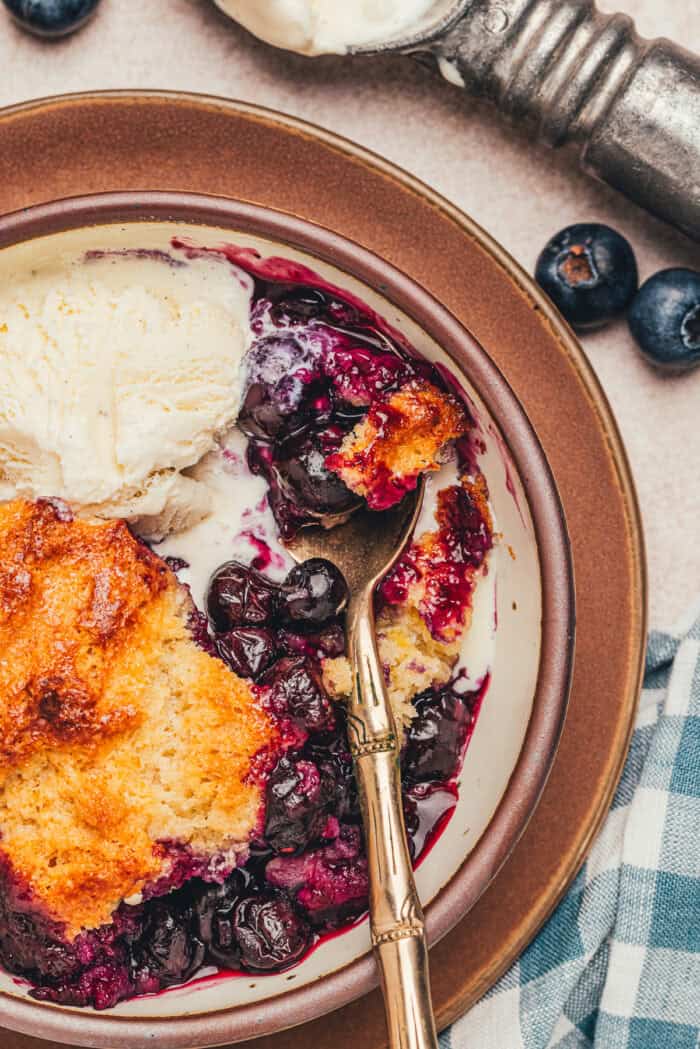 A bowl with a serving of blueberry cobbler and a spoon.
