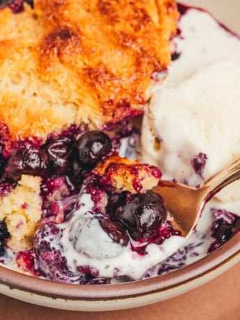A bowl with a serving of blueberry cobbler and a spoon.