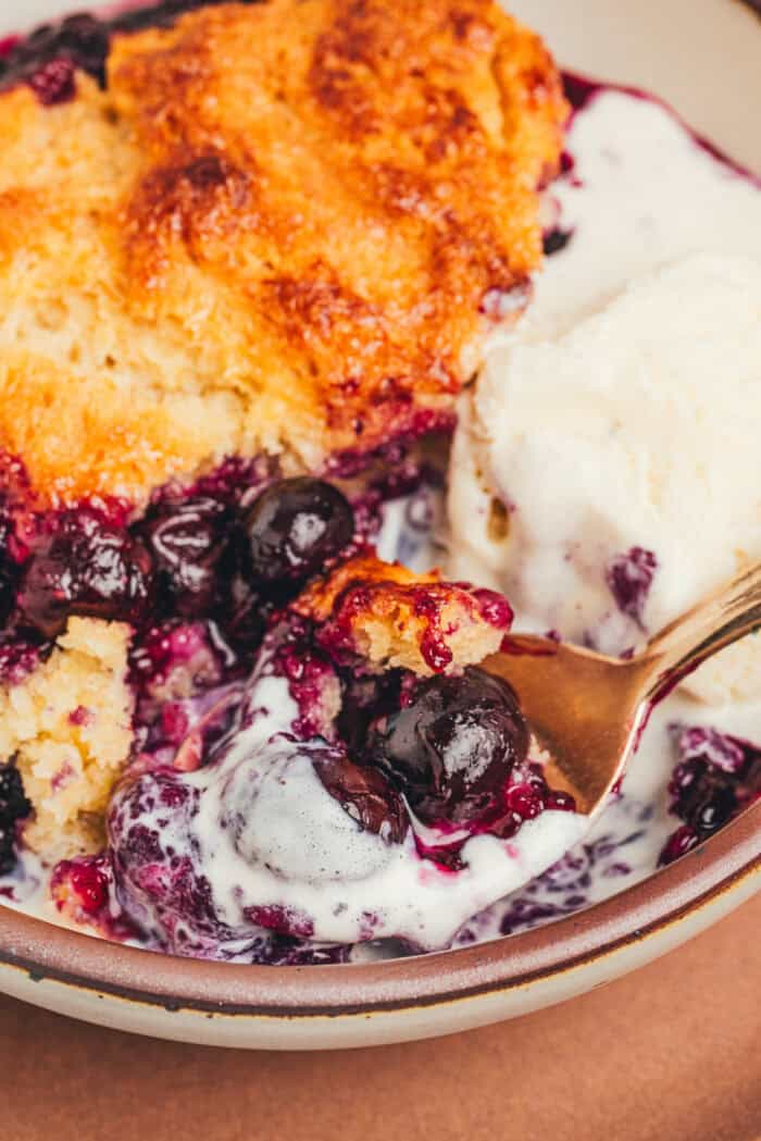 A bowl with a serving of blueberry cobbler and a spoon.