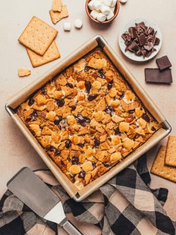 A square baking pan with S'mores bars and the ingredients used to make them around the baking pan.