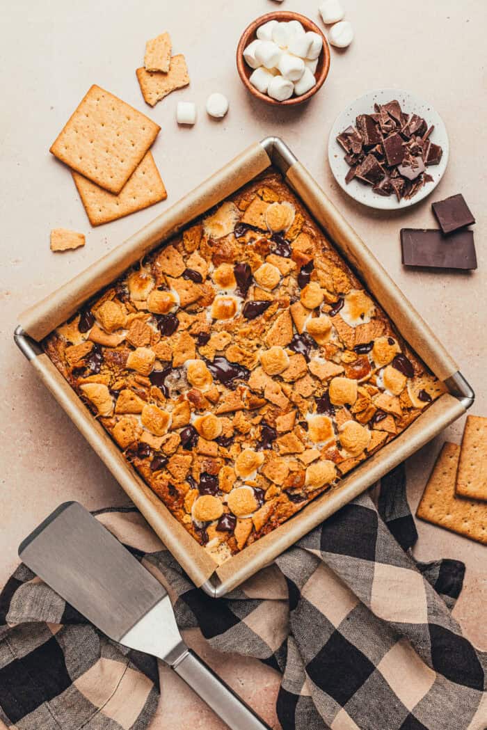 A square baking pan with S'mores bars and the ingredients used to make them around the baking pan.
