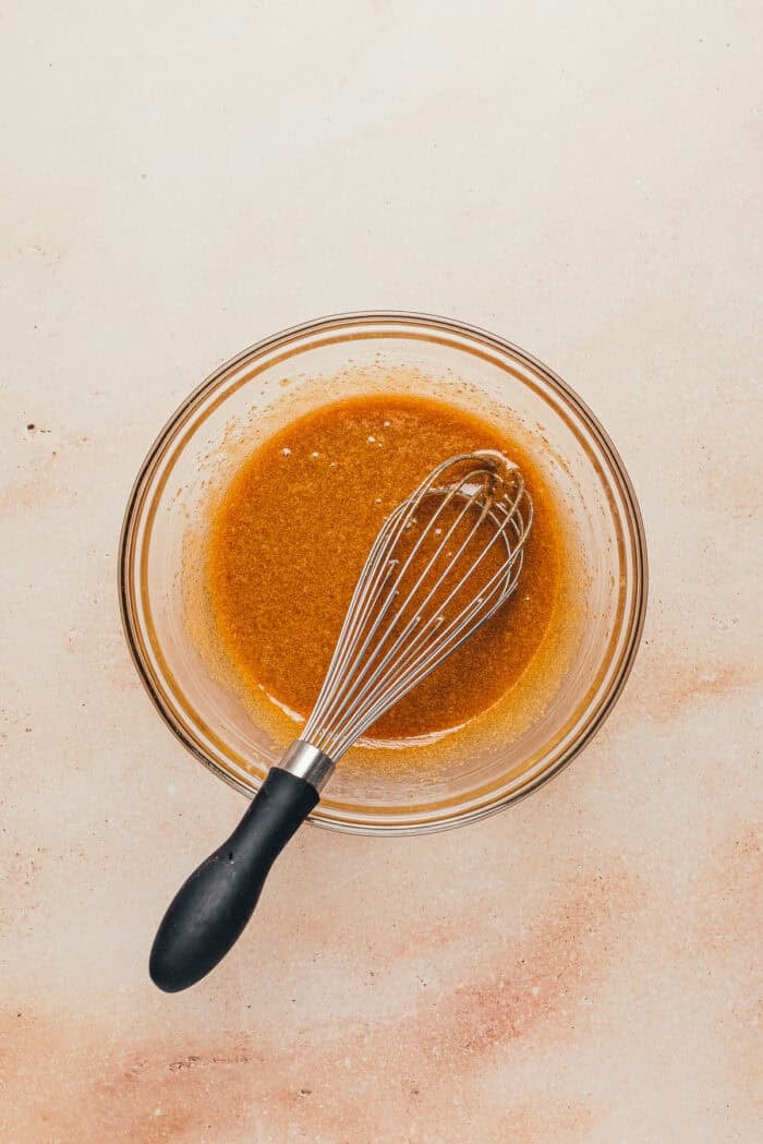 A glass bowl with the wet ingredients mixed together with a whisk.