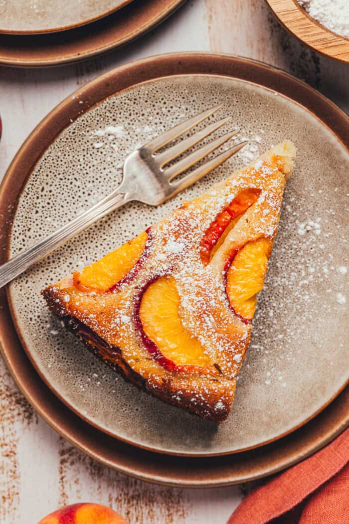 A slice of homemade peach cake on a plate with a fork.
