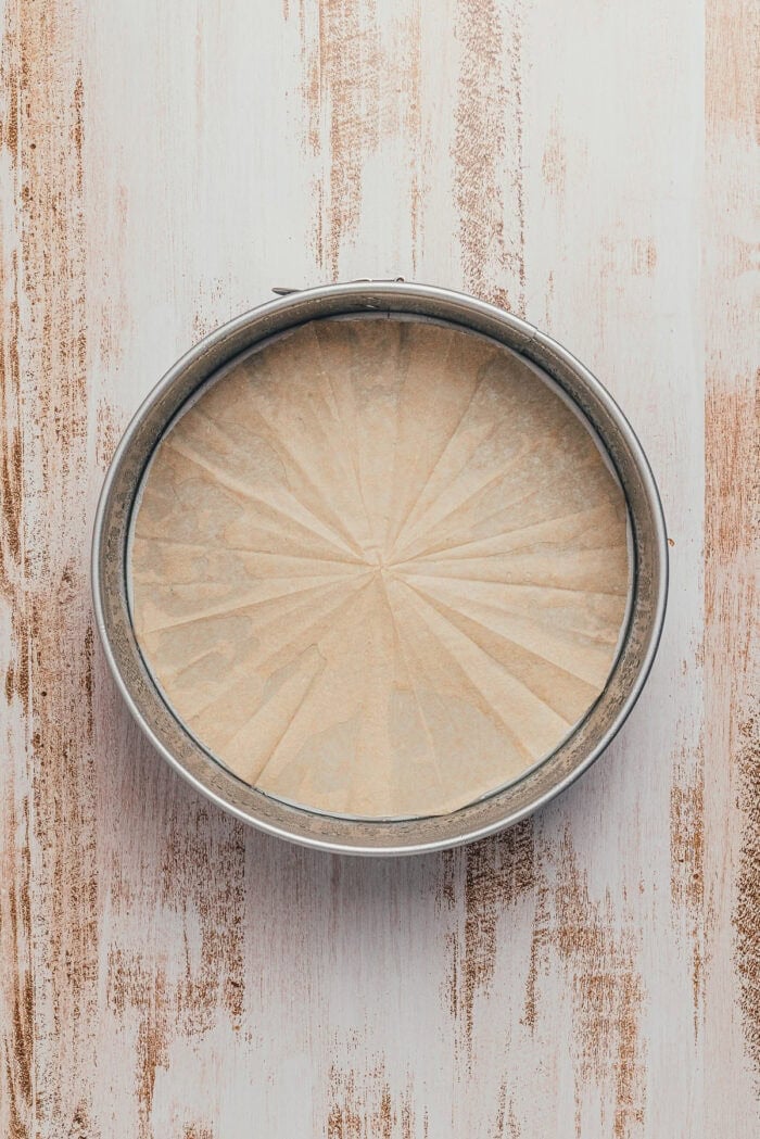 A round cake pan that has been greased with parchment paper.