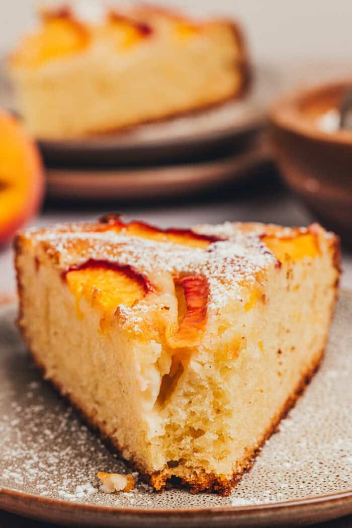 A slice of peach snack cake with a bite taken out of it on a plate.