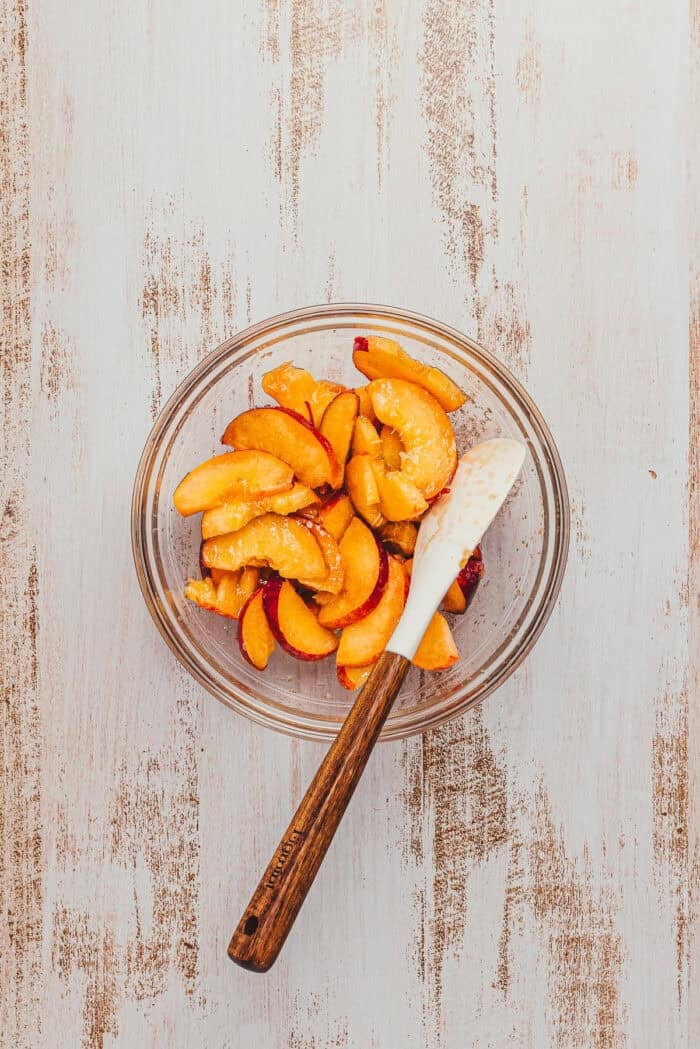 Fresh sliced peaches in a bowl with a spatula.