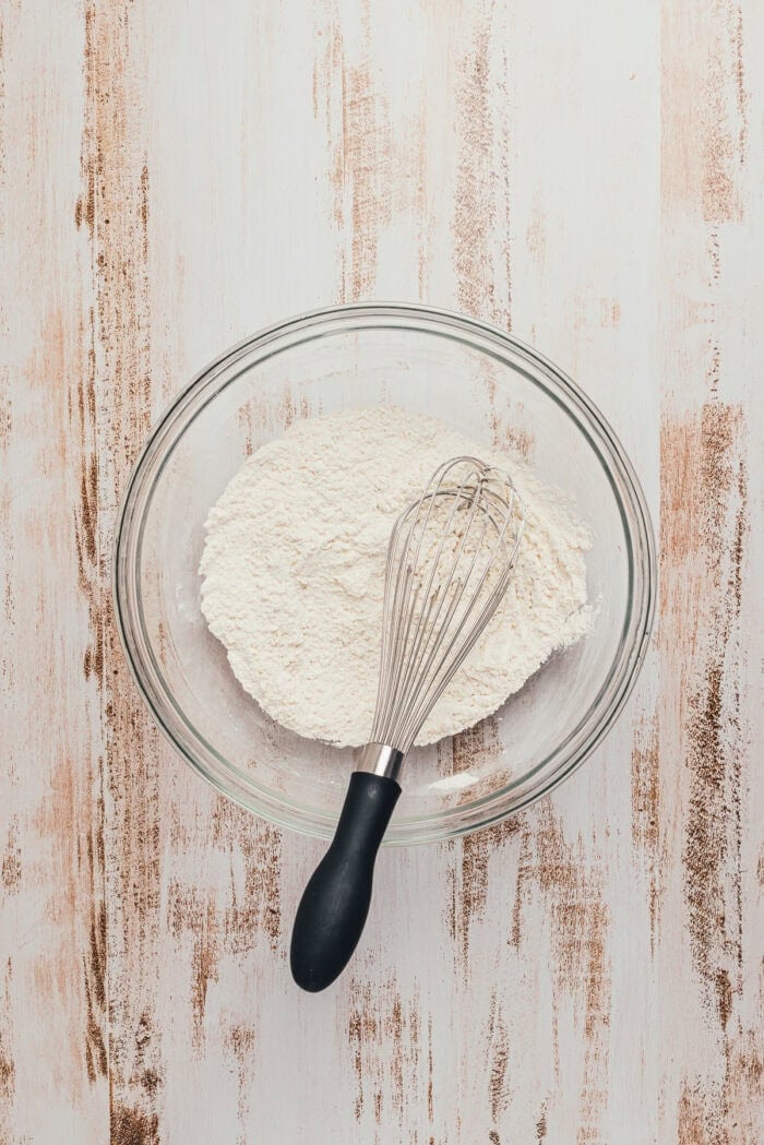 A glass bowl with the dry ingredients and a whisk.