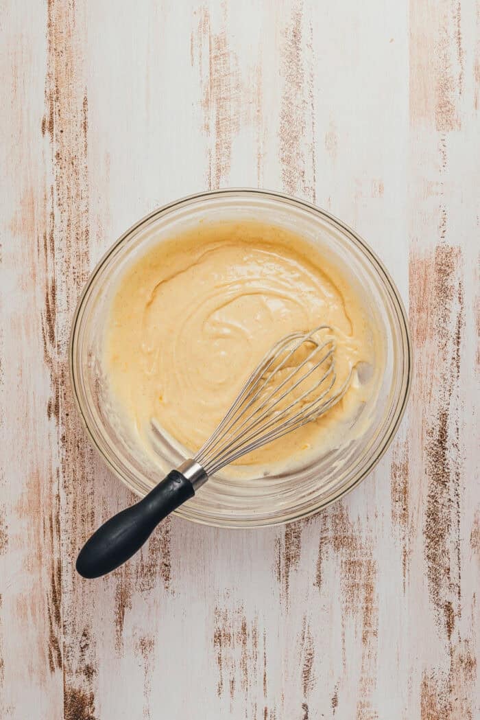 Cake batter mixed together in a glass bowl with a whisk.