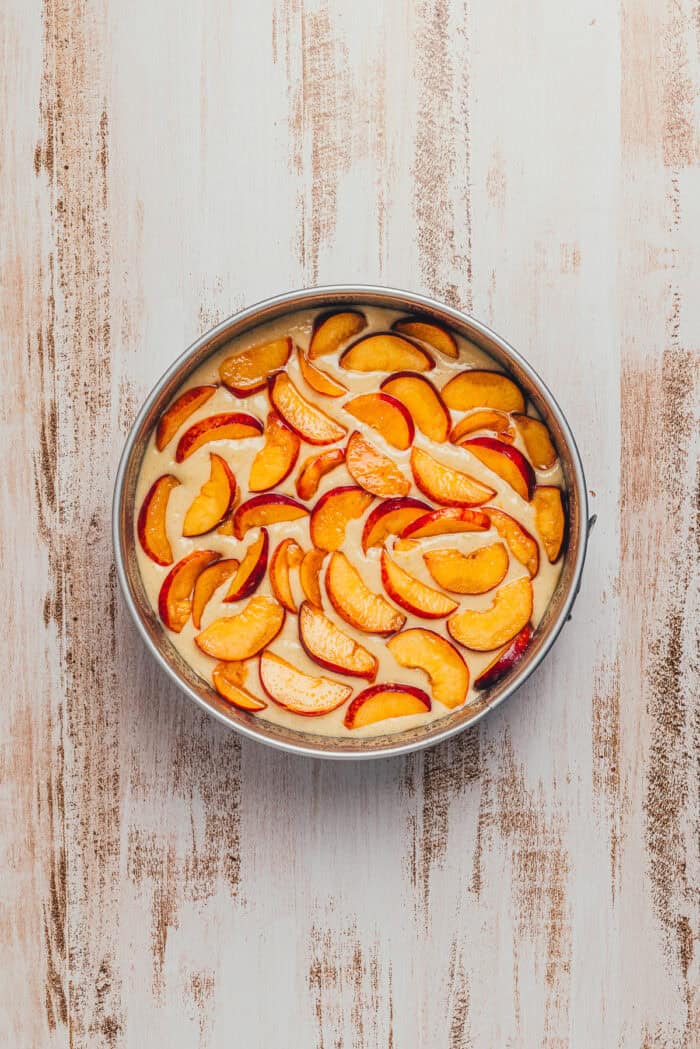 Sliced peaches layered on cake batter in a round cake pan.