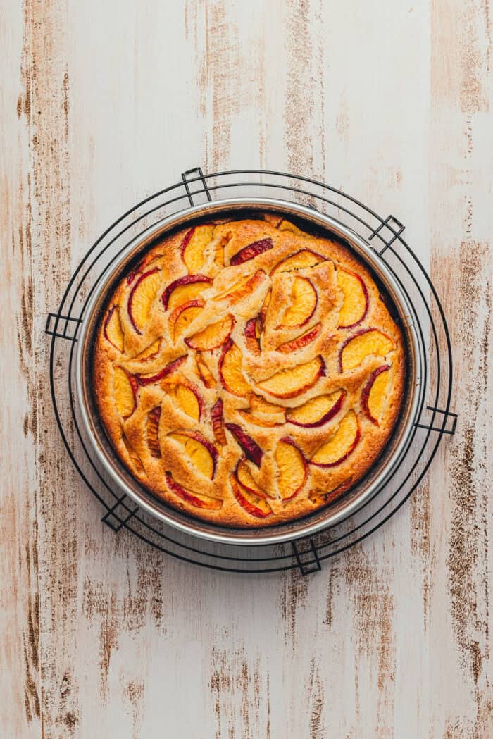 A baked peach snack cake cooling in the cake pan on a cooling rake.