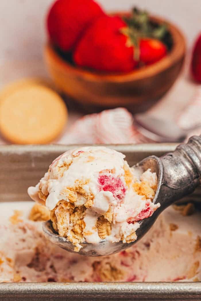 A scoop of homemade strawberry ice cream being scooped out of the container.