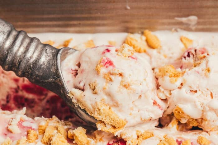 A scoop of homemade strawberry ice cream being scooped out of the container.