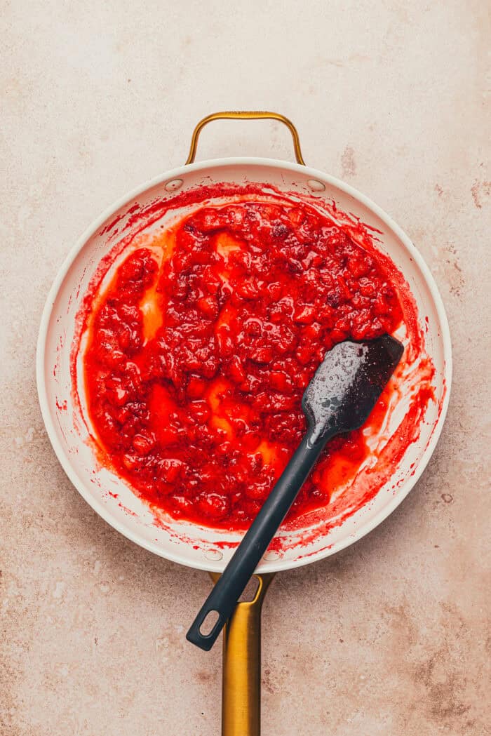 Cooked strawberries in a pan with a spatula.