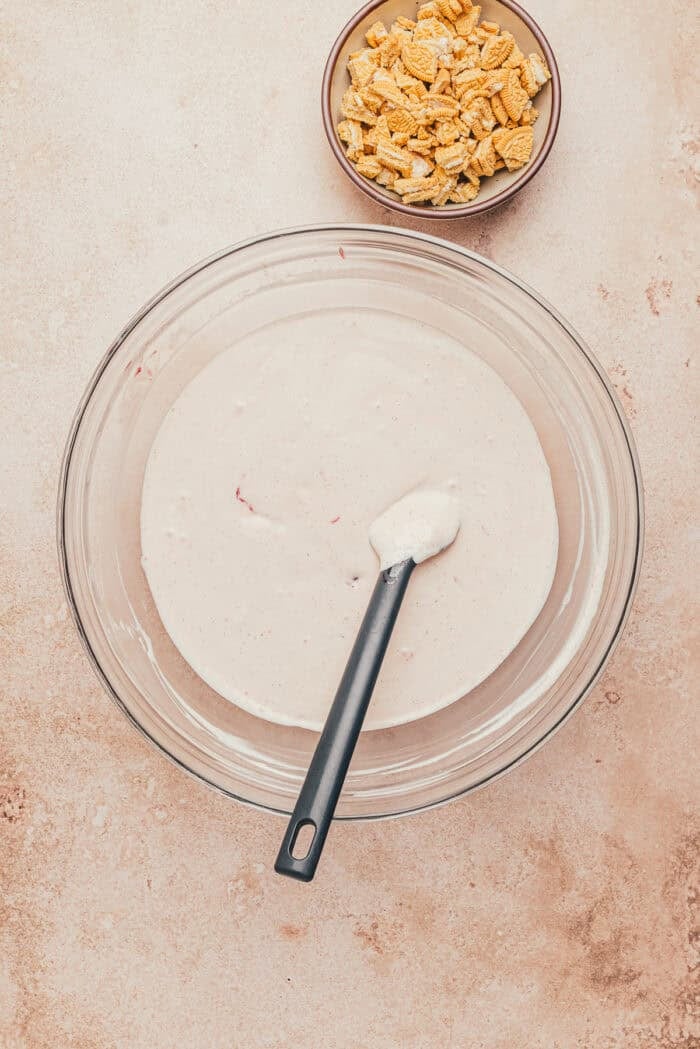 Heavy whipping cream mixed with the strawberry condensed milk mixture in a glass bowl.
