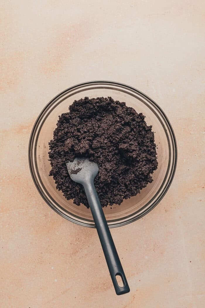 A glass bowl with Oreo cookie crumbs and melted butter.