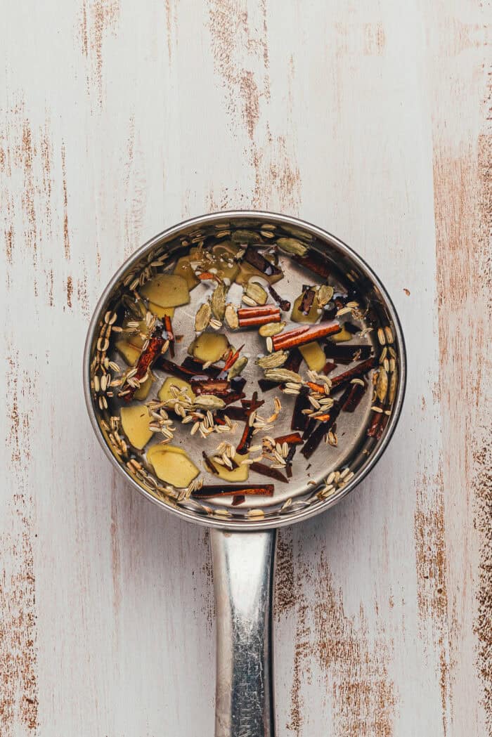 Pot of chai syrup with cinnamon sticks, cardamom, and ginger simmering on the stove