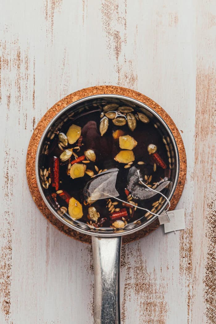 Pot of chai syrup with cinnamon sticks, cardamom, and ginger simmering on the stove