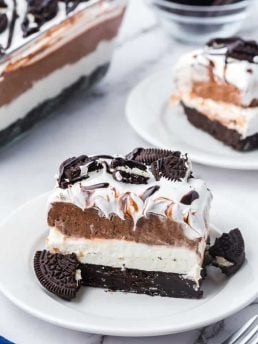 Two plates with slices of no bake Oreo layered dessert with the glass dish with the dessert in it in the background.