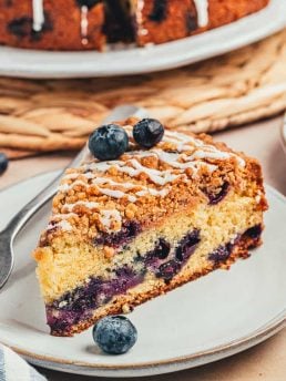 A slice of blueberry sour cream coffee cake on a white plate with a fork.