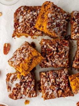 Baked pumpkin pecan coffee cake that has been removed from the cake pan with icing drizzled all over it and sliced into squares.