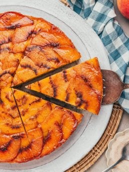 A slice of peach upside down cake being removed from the whole cake.
