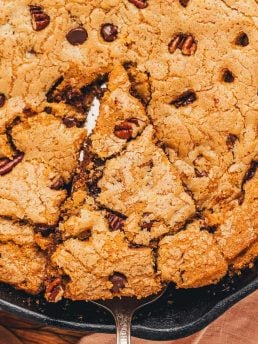 A slice of chocolate chip cookie being lifted out of the main dish.