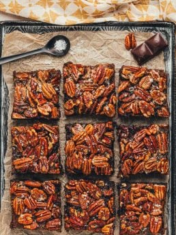 Brownies with a pecan pie topping are sliced and displayed on parchment paper.