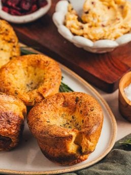 A few brown butter popovers on a platter with a bowl of butter in the background.