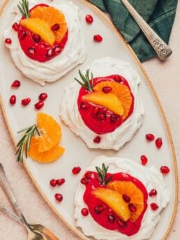 Three mini pavlovas with cranberry curd and orange slices with other garnishes on a platter.