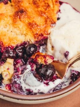 A bowl with a serving of blueberry cobbler and a spoon.